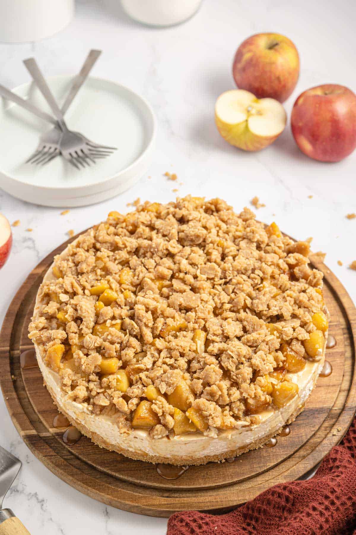 An apple crisp cheesecake on a wooden cutting board.