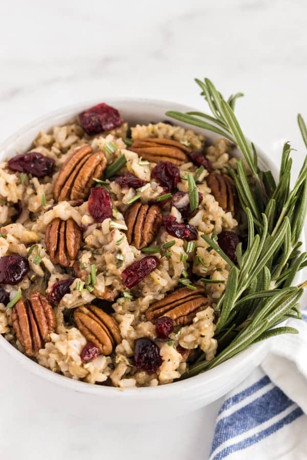 brown rice pilaf in a white bowl with rosemary, pecans and cranberries