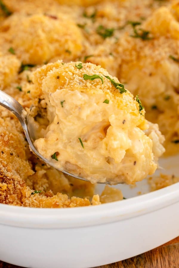 Cheesy cauliflower au gratin in a white dish with a spoon.