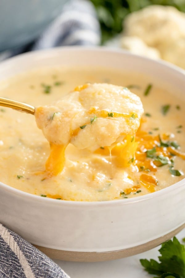 cauliflower cheese soup in a white bowl with a spoon.