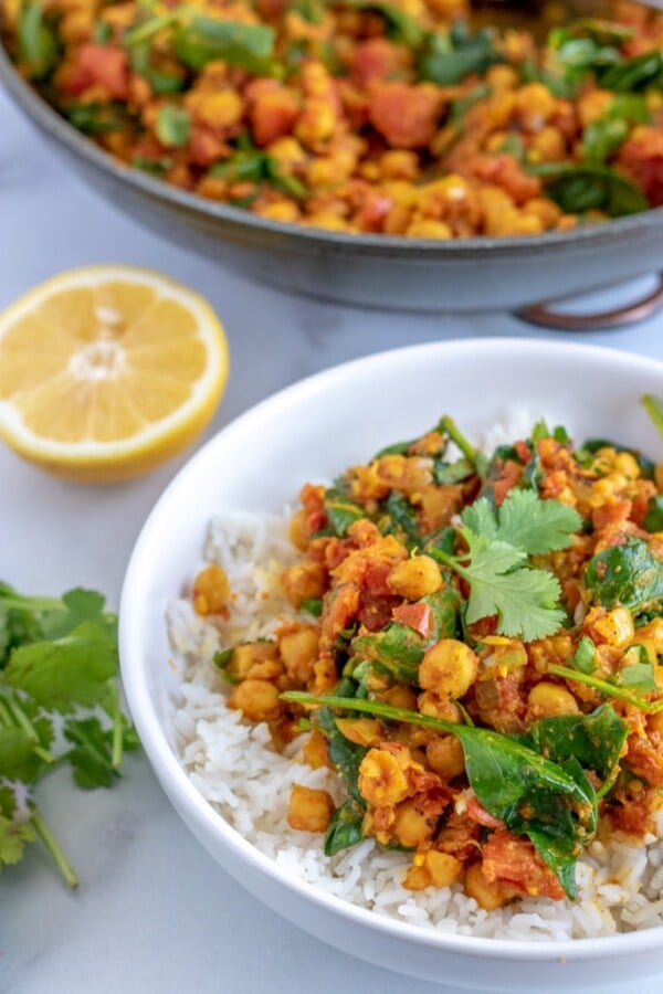 chickpea curry in a white bowl with a cut lemon