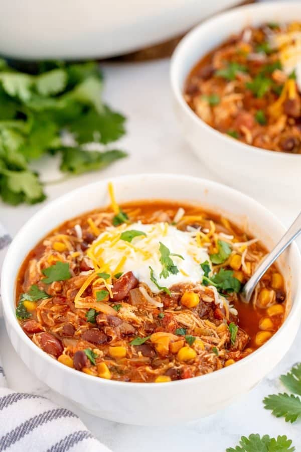 bowl of chicken chili with sour cream, cheese and cilantro on top