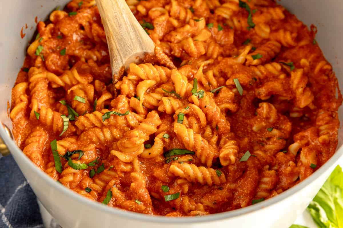 tomato chicken pasta in a bowl with a wooden spoon.