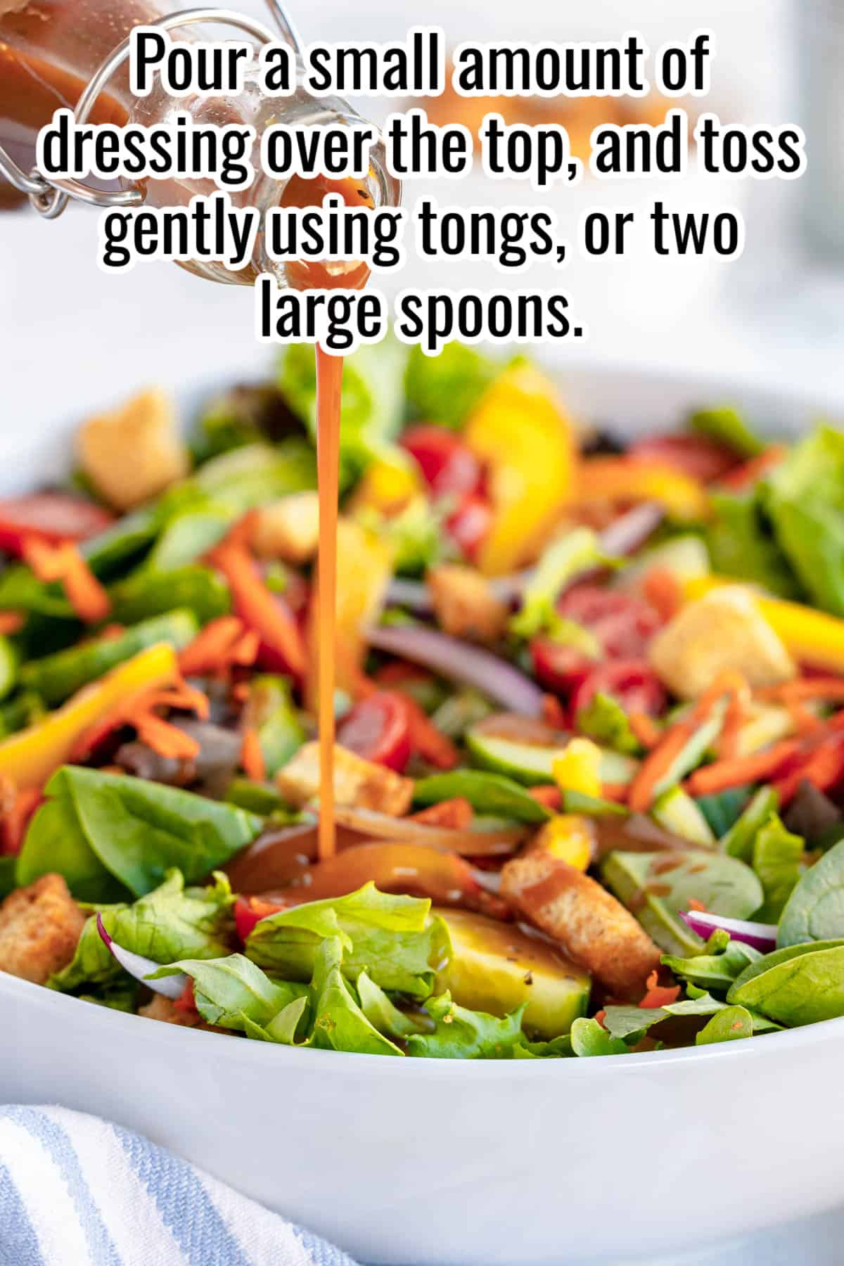 garden salad in a white bowl with the words "Pour a small amount of dressing over the top and gently using tongs or large spoons"