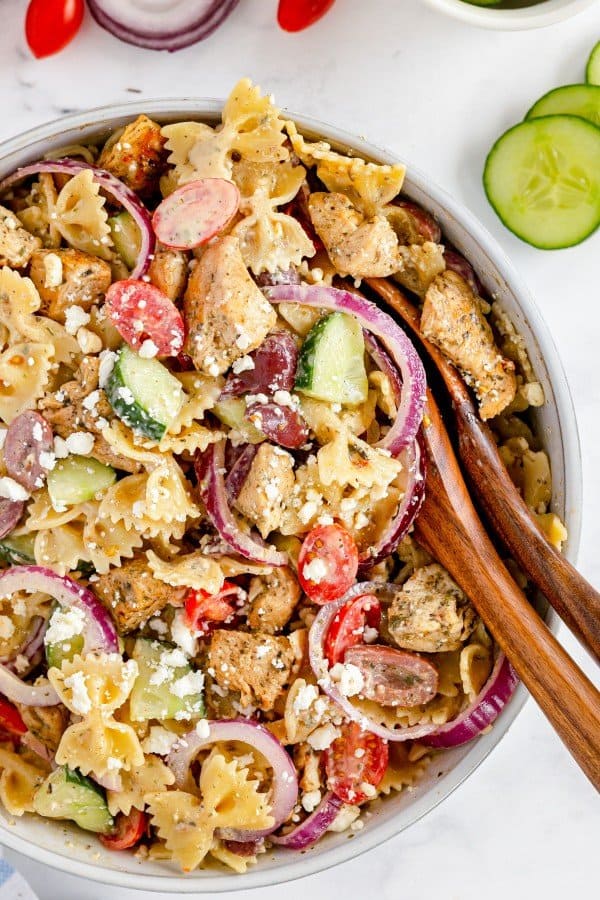 greek pasta salad with wooden serving spoons and veggies