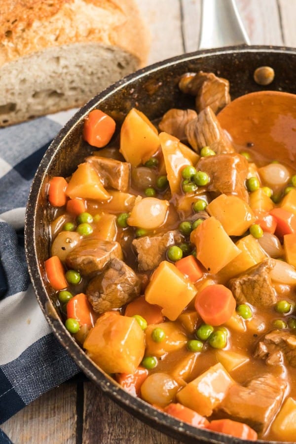 stove top beef stew in a skillet with a wooden spoon.