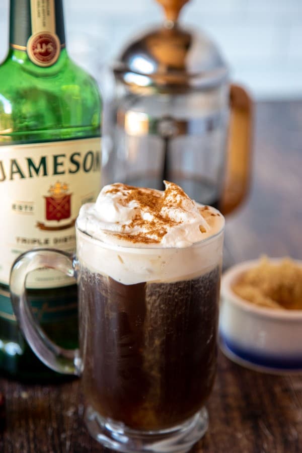 Irish coffee with a whiskey bottle, sugar and coffee in the background