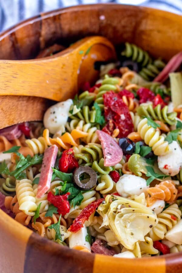 Antipasto salad in a wooden bowl with spoons.