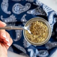 italian seasoning in a jar, with a blue napkin and a spoon