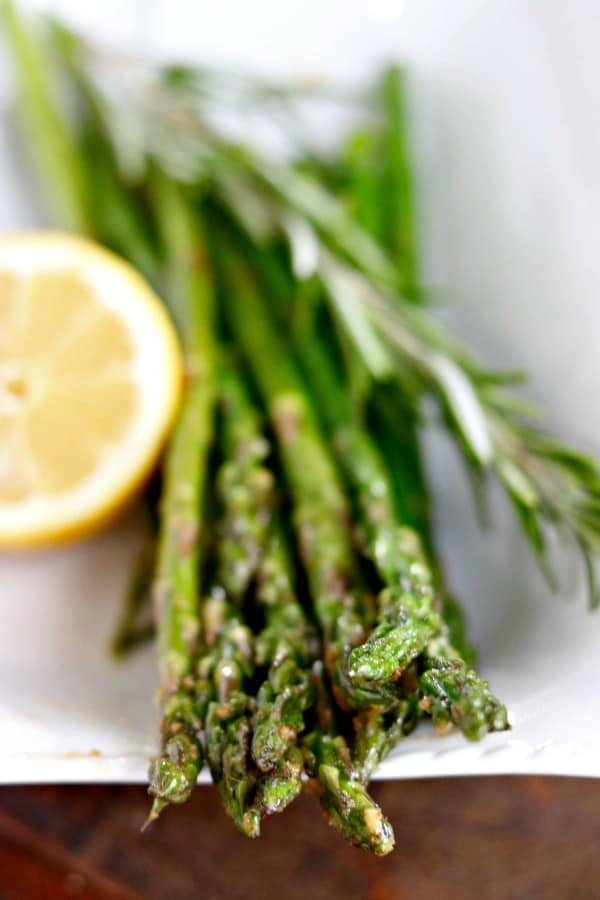 asparagus with lemon and rosemary in a white dish.
