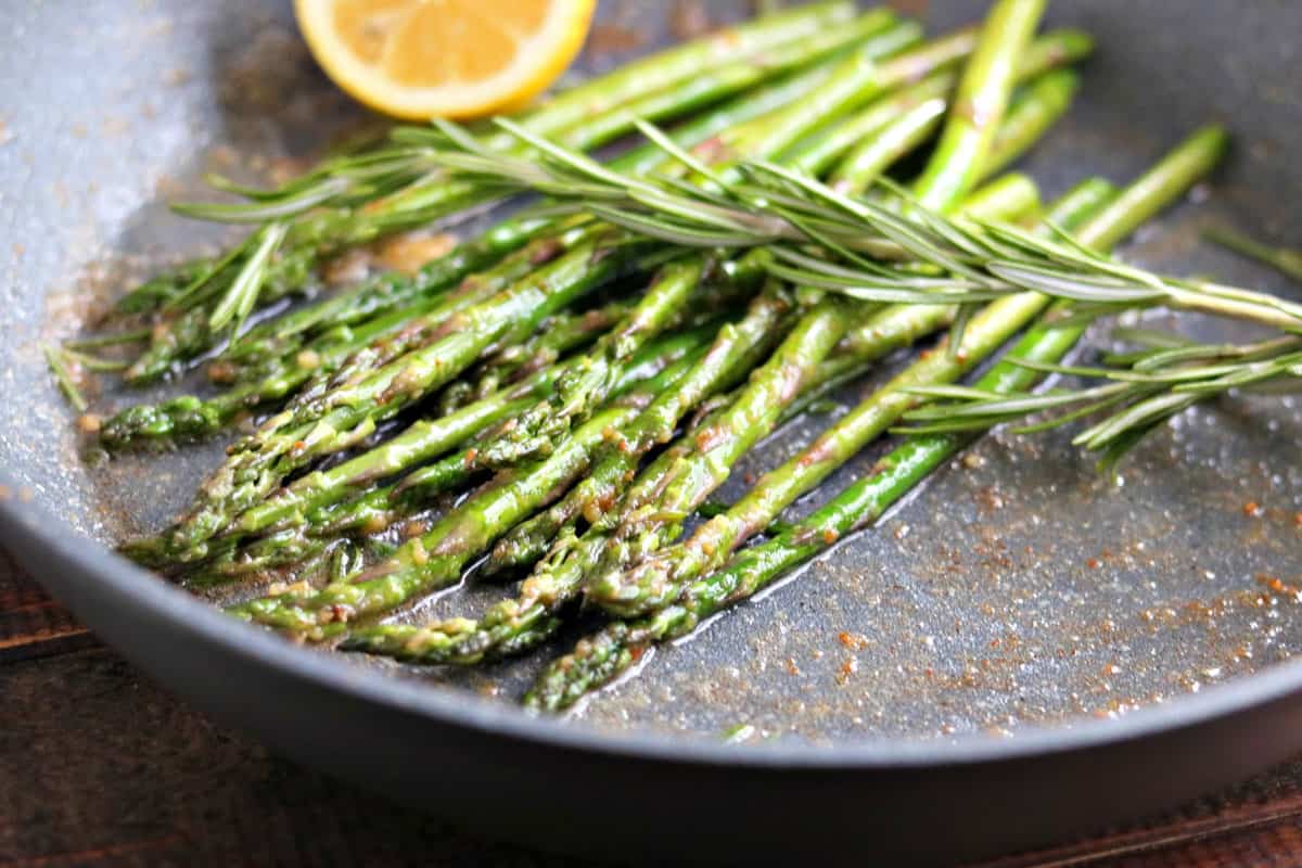 a skillet with cooked asparagus in it with lemon and rosemary.