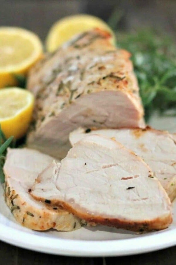 pork tenderloin slices on a white plate with lemons and rosemary