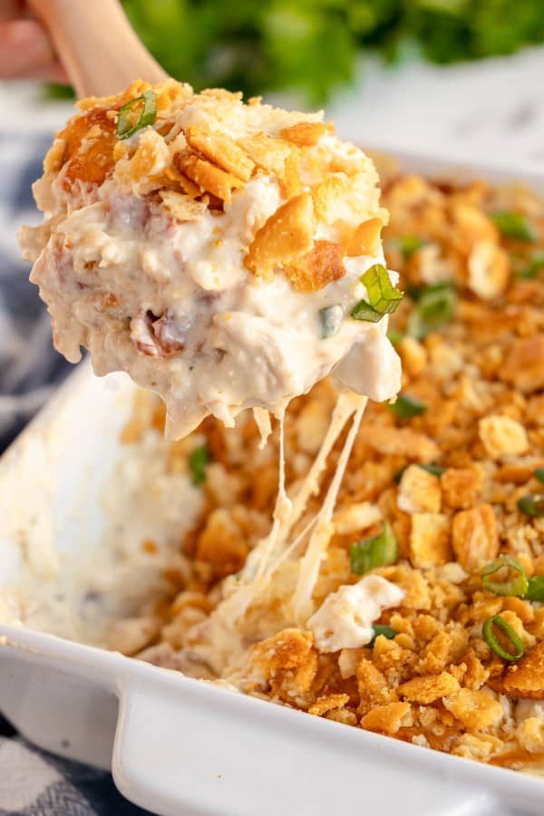 Taking a spoonful of Million Dollar Chicken Casserole out of a casserole dish.