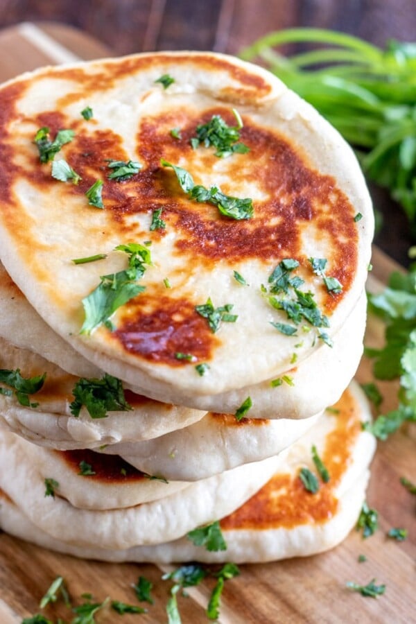 golden naan bread with cilantro stacked on a wooden board.