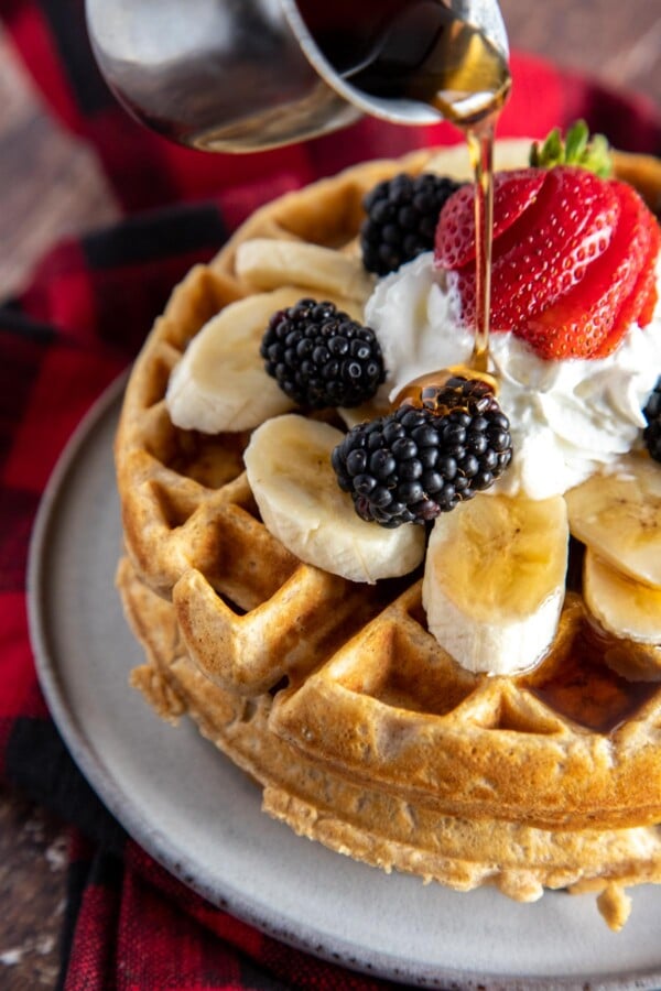 syrup being poured over fruit topped waffles