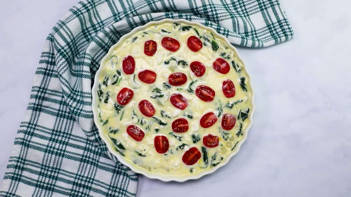 quiche batter in a tart pan, unbaked with feta and halved tomatoes on top.