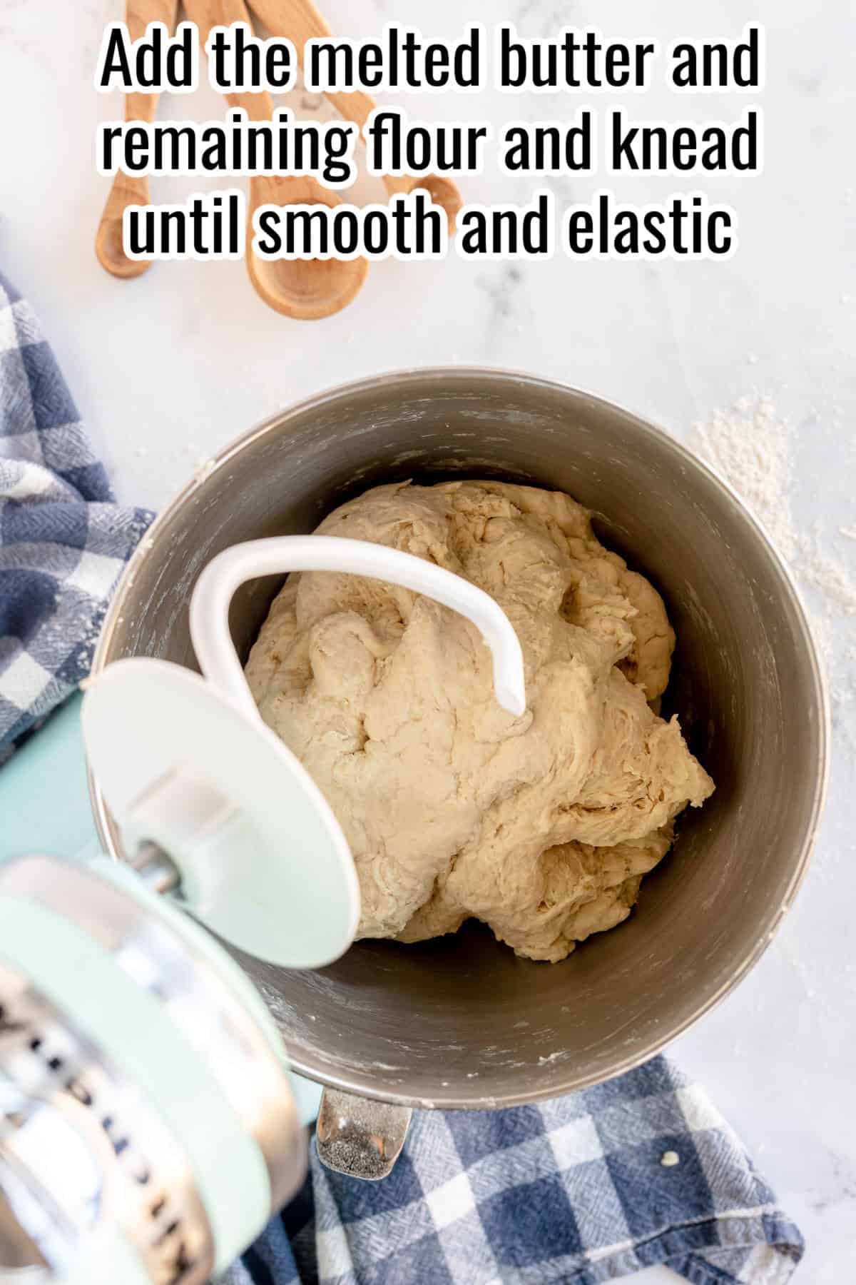 A dough mixer bowl with dough, a dough hook attachment, and a checked cloth nearby. The text reads, "Add the melted butter and remaining flour and knead until smooth and elastic for perfect sandwich bread".