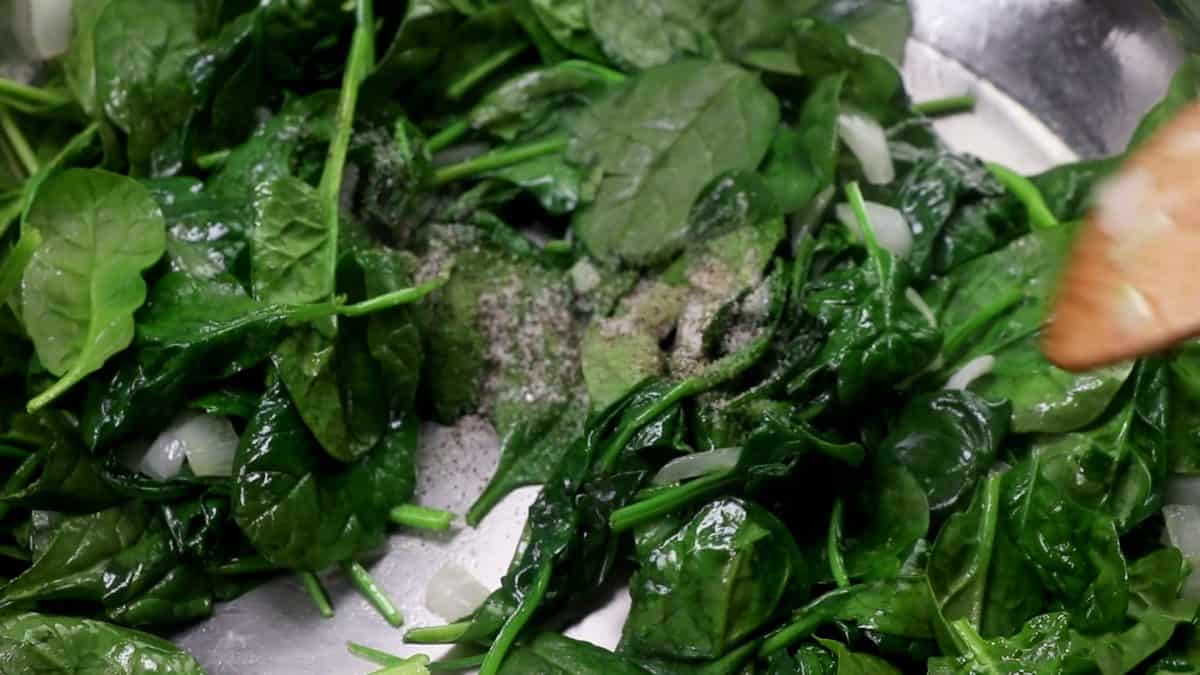 fresh spinach in a skillet with a wooden spoon, with pepper.