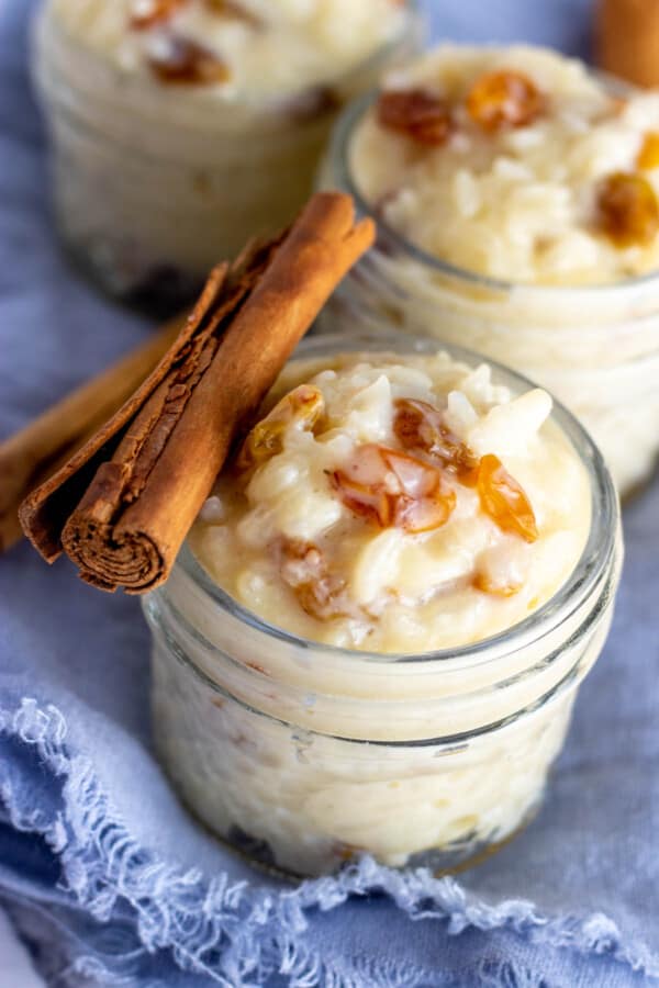 rice pudding in glass jars with cinnamon sticks laid across the top