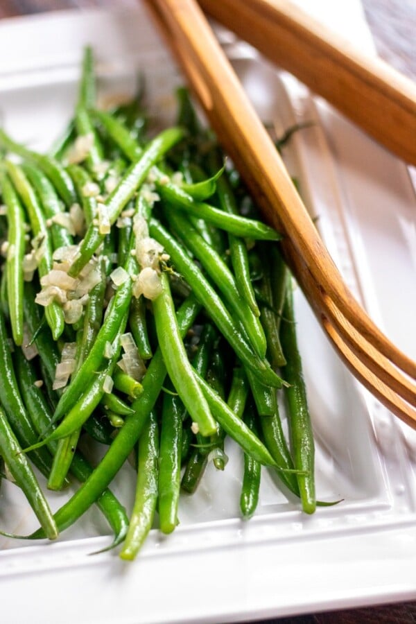 sauteed green beans on a white platter with wooden tongs
