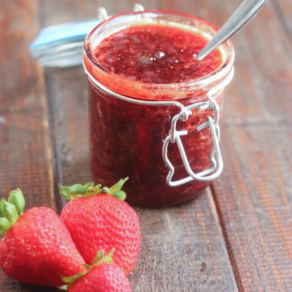 jar of strawberry jam with a spoon in it with strawberries alongside it