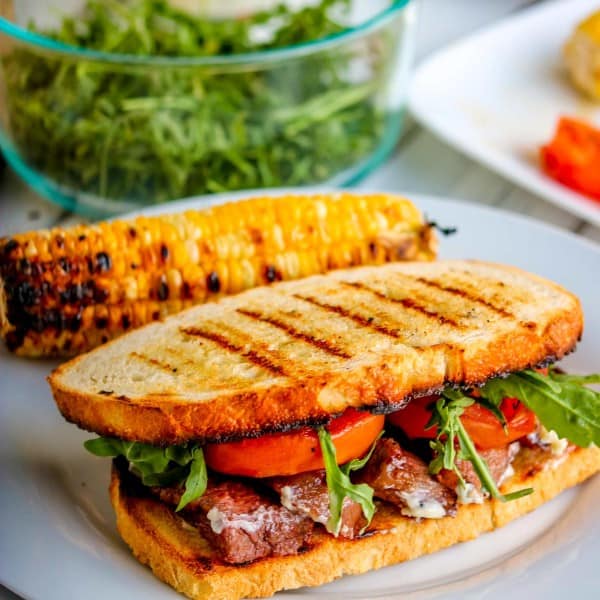 a steak sandwich with grilled bread on a white plate.