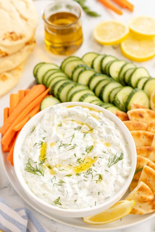 tzatziki greek yogurt dip on a platter with cucumbers, carrots and pita dippers.