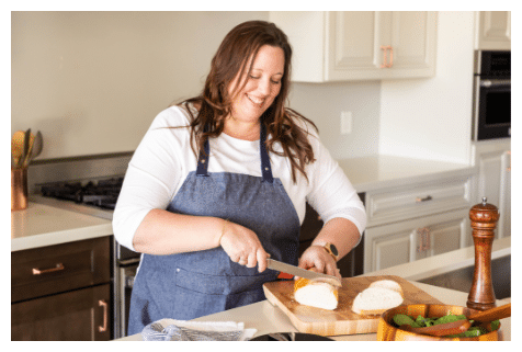 Kylee in the kitchen with knife, cutting bread.
